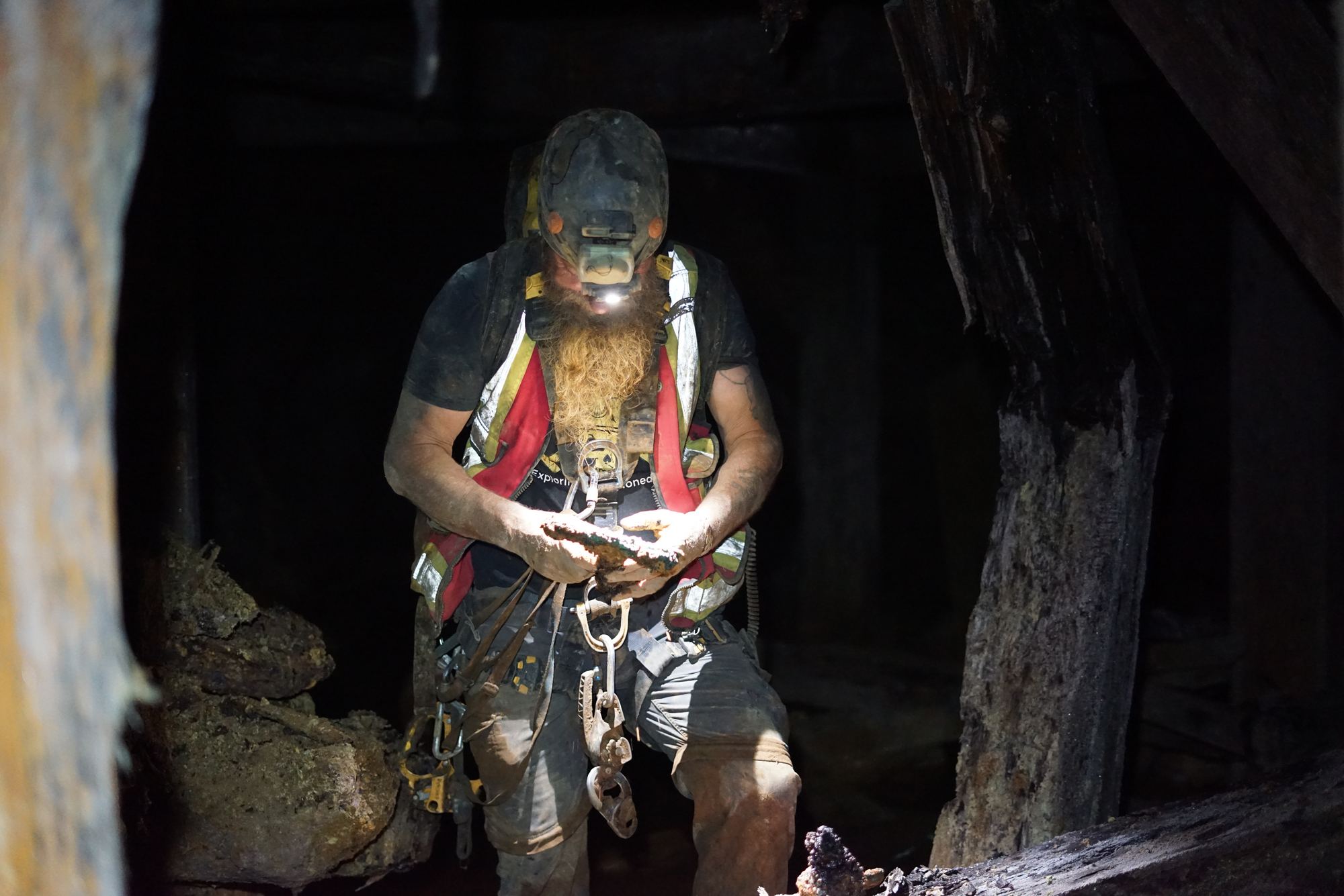 Frank Schlichting underground in his harness and hi-vis vest, his headlamp lighting a rusted relic in his hands, old timbers all around