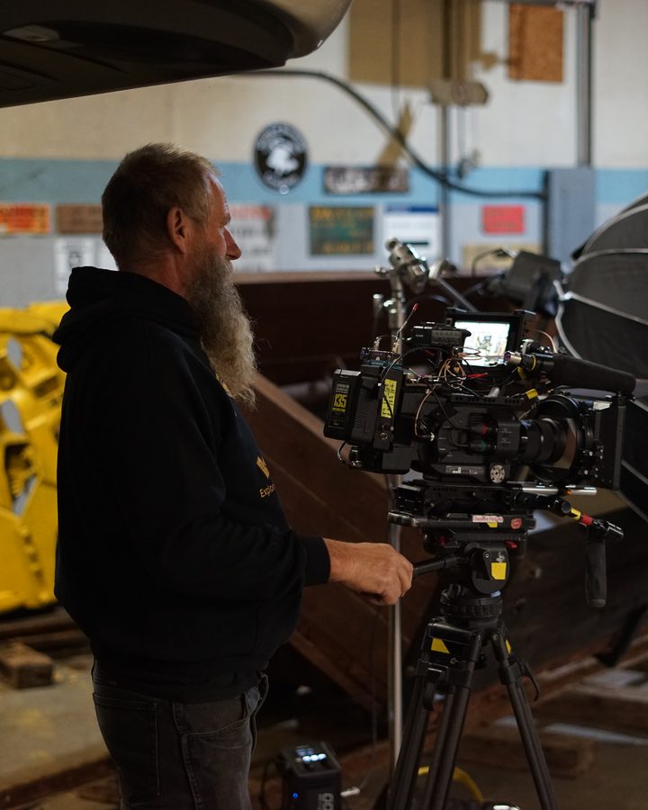 Frank Schlichting behind a cinema camera on a tripod, a large round softbox light beside it