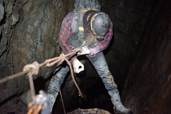 Frank on a rope in a dark shaft, red plaid shirt, headlamp on