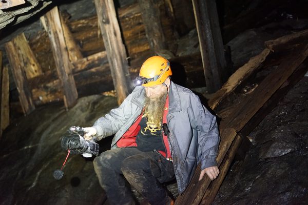 Frank filming with his camcorder, sitting on the old timbers of a stope