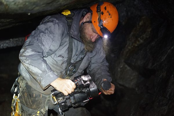 Frank with his camcorder in a tight, wet passage, headlamp on