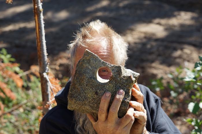 Frank holding a block of rock up to his face, one eye looking through a round hole drilled clean through it