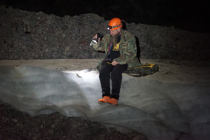 Frank sitting on a ledge of ice deep in an abandoned mine, his headlamp lighting the ice
