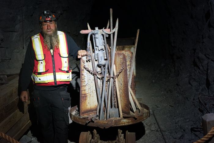 Frank beside an old ore car loaded with rusty rock drills, drill steel and shovels