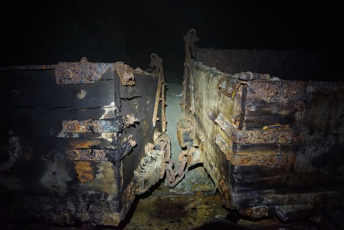 Two rusted ore cars on old rails in the dark of an abandoned mine