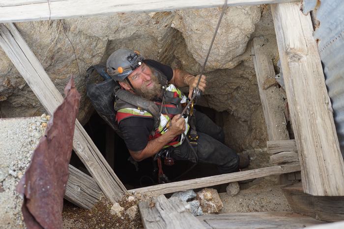 Frank Schlichting on a rope in a timbered mine shaft, looking up at the camera