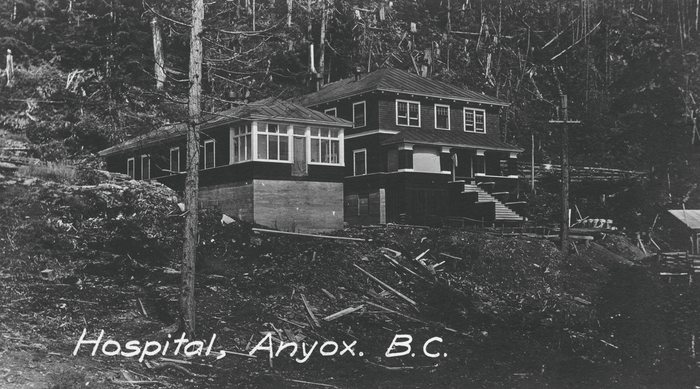 An old postcard of the hospital at Anyox, BC: a long two-storey frame building with a glassed sun porch on a cleared hillside of stumps, felled trees behind; printed on it, &ldquo;Hospital, Anyox. B.C.&rdquo;