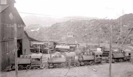 A line of small steam and electric locomotives outside the roundhouse at Anyox, BC, in 1917, bare hills behind