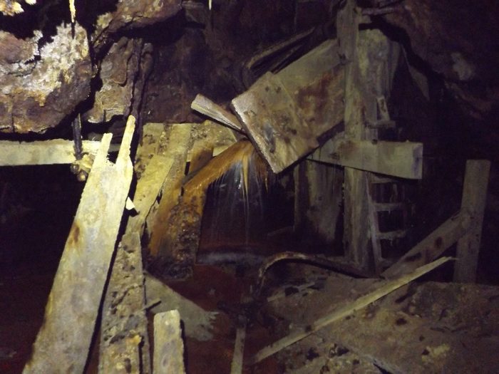 Orange mine water pouring through broken chute timbers in the Hidden Creek mine at Anyox, BC, a ladder behind