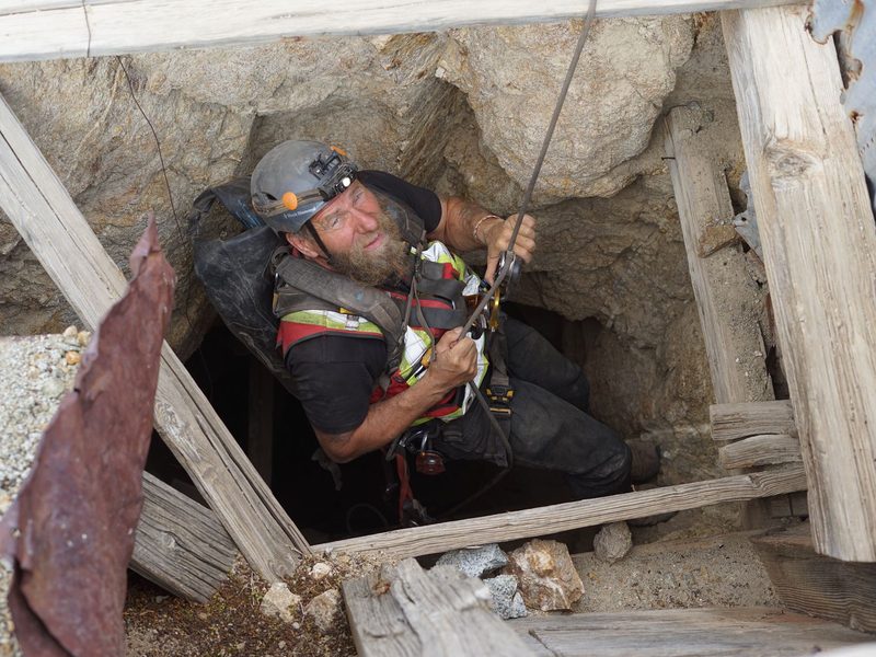 Frank Schlichting in a helmet, hi-vis vest and harness, on a rope in an old timbered shaft, looking up