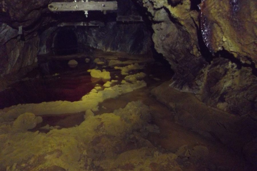 A flooded drift in the Hidden Creek mine at Anyox, BC: yellow mineral crusts rising out of red water under old timbers, the drift running on into the dark