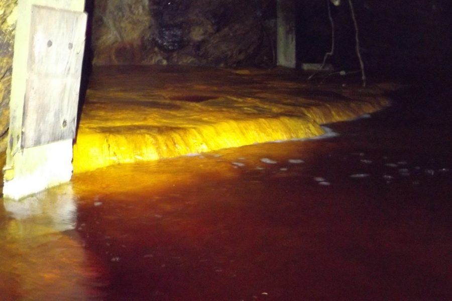 Mine water spilling amber over a natural mineral dam in the Hidden Creek mine at Anyox, BC, beside an old timber post