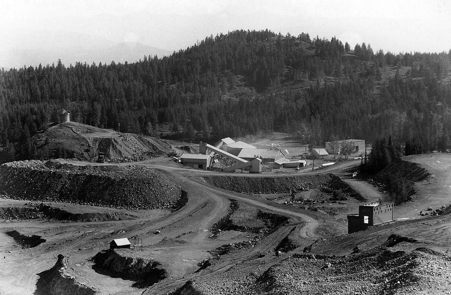 The Phoenix pit in July 1965, from the headwall of the old Ironsides: benches and haul roads, Granby’s concentrator beyond, and two relics of the first mine at Phoenix, BC: the pumphouse at the collar of the Victoria shaft, lower left, and the old substation, lower right