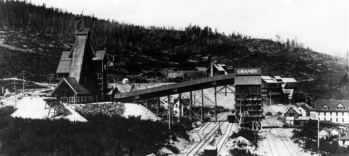 The Victoria shaft at Phoenix, BC, in 1907: the timber headframe flying a flag, a covered conveyor running to the Granby ore bins, rail tracks below and houses of the town at the right