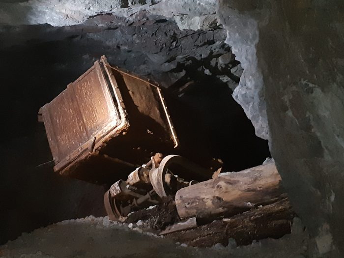 A rusted ore car lying on its side with its wheels showing, in a dark drift at Phoenix