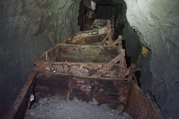 A line of rusted ore cars standing on the rails in a narrow drift at Phoenix