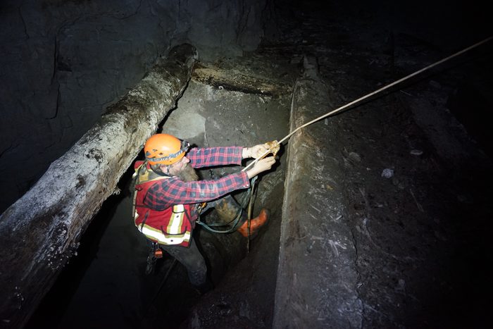 Frank in an orange helmet and plaid shirt setting a rope among heavy stope timbers at Phoenix
