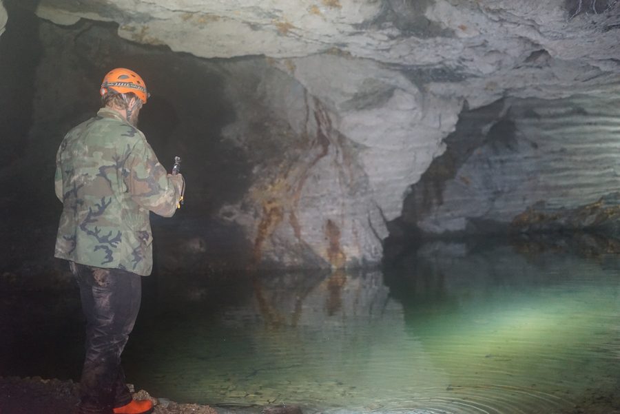 Frank in a camouflage jacket and orange helmet standing at the edge of still green water that fills an old drift at Phoenix