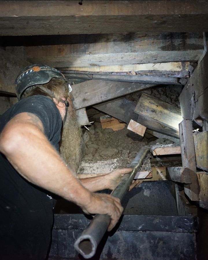 Frank working a steel bar at a timbered chute, muck spilling toward the ore car below