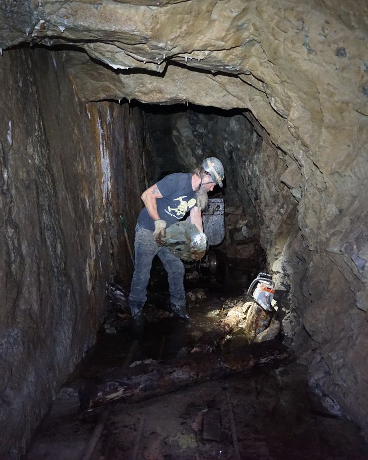 Frank carrying a heavy rock through a narrow drift, the ore car behind him