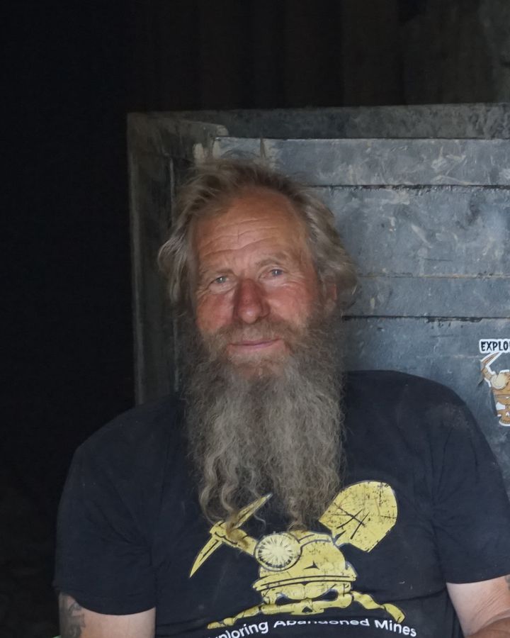 Frank Schlichting smiling in front of an ore car, in an Exploring Abandoned Mines T-shirt